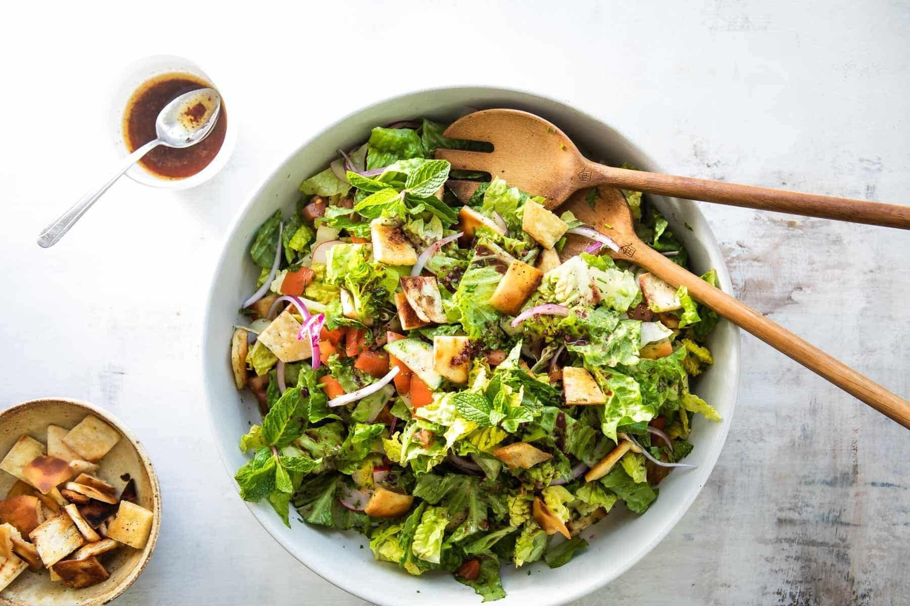 Fattoush in a white bowl with wooden serving utensils.