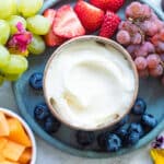 A small brown bowl of fruit dip surrounded by various fruits.