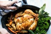Someone holding a garlic butter roast chicken in a black roasting pan.