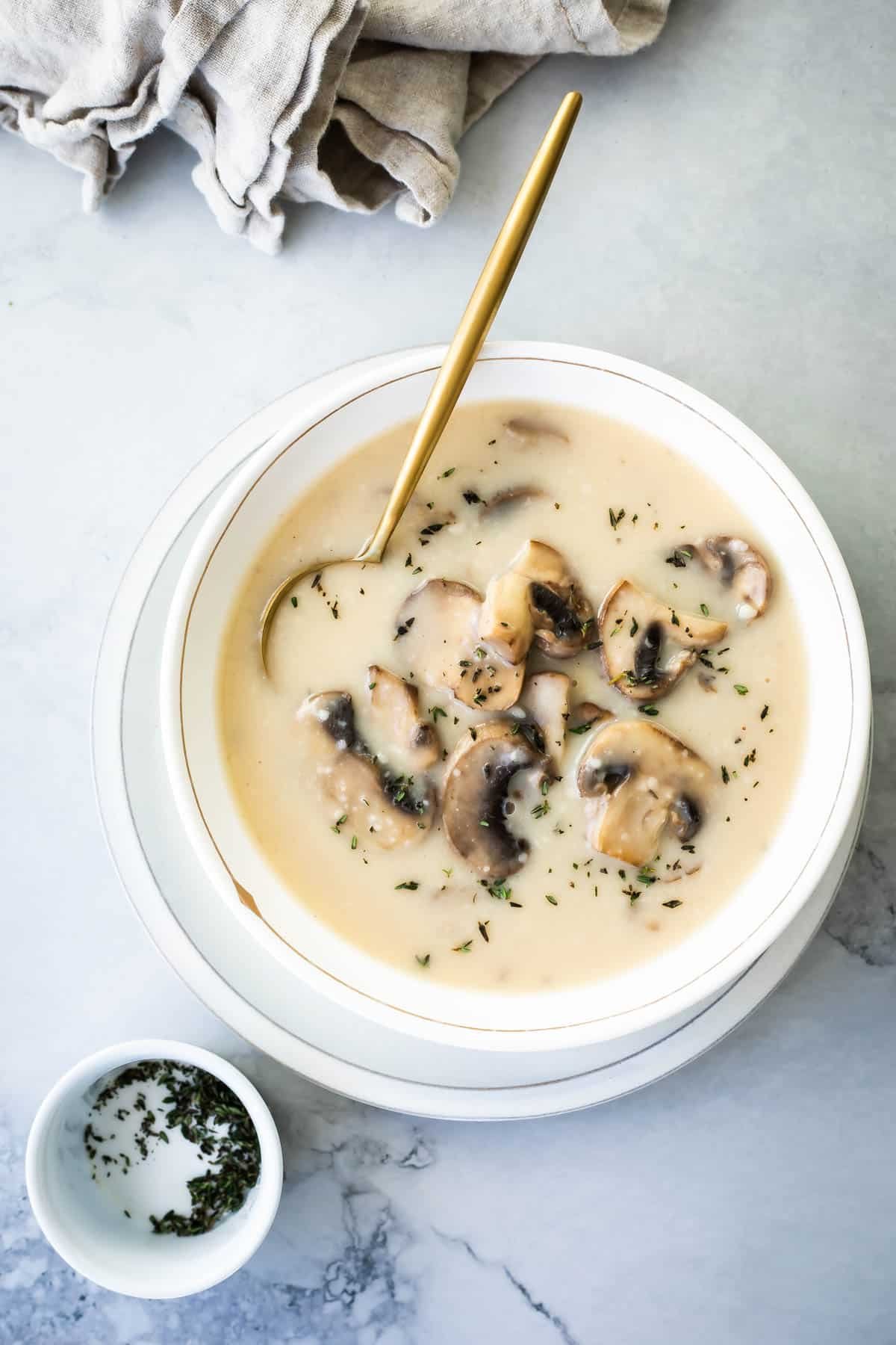 Homemade cream of mushroom soup in a white bowl with a gold spoon.