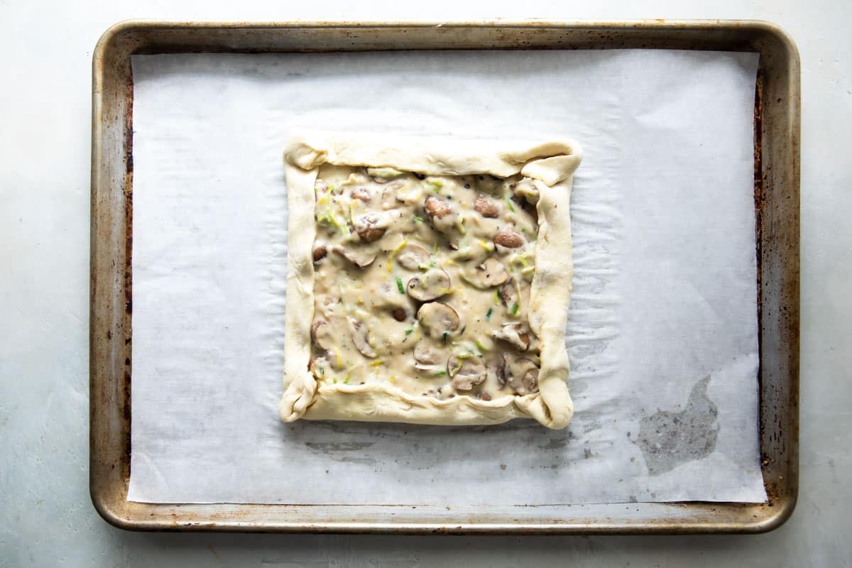 An unbaked mushroom and leek tart on a baking sheet.