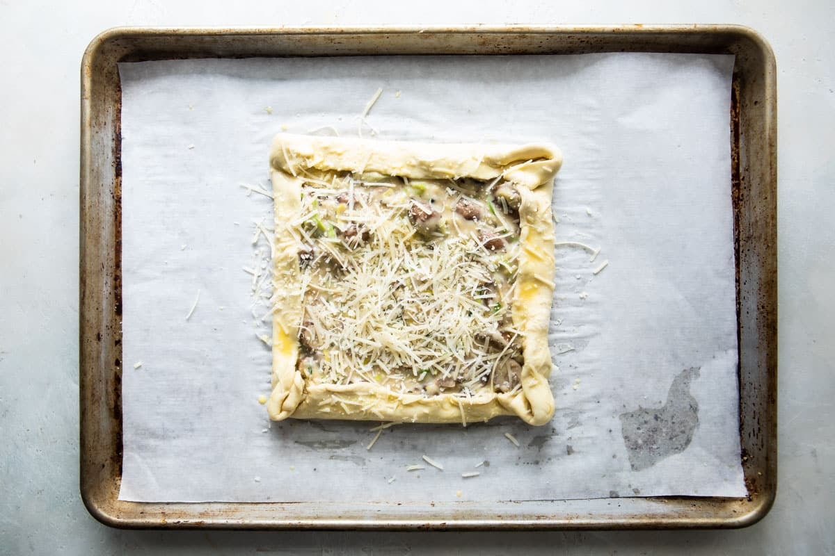 An unbaked mushroom and leek tart on a baking sheet.