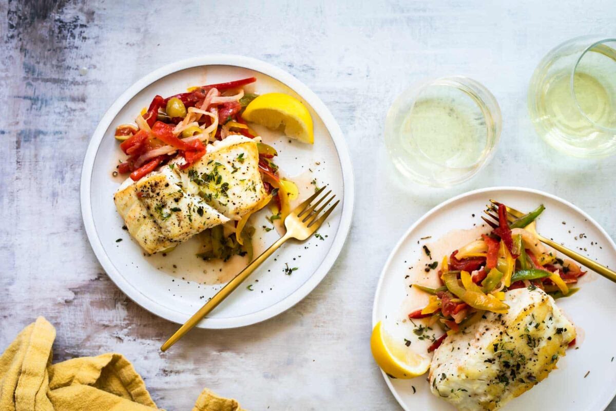 Two plates with pan-seared halibut, peppers and olives.