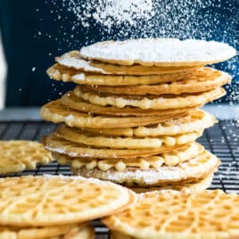 Pizzelle cookies being dusted with powdered sugar.