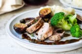 A plate with mashed potatoes, broccoli and pork tenderloin with figs.