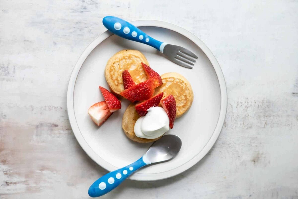A plate with pancakes, strawberries, and whipped cream on it.