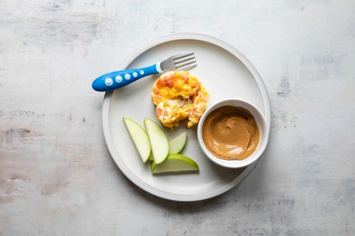 A plate with an egg cup, peanut butter, and apples on it.