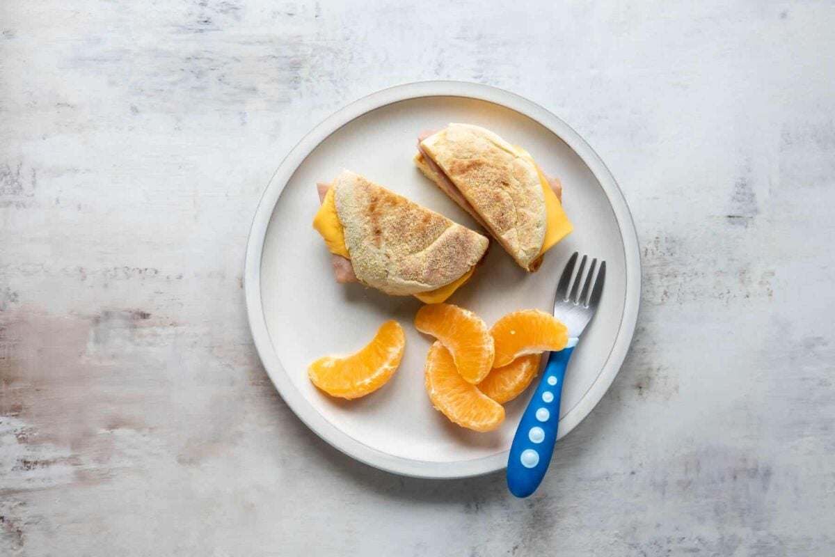 A plate with a breakfast sandwich and mandarin oranges on it.