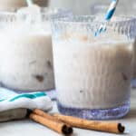 Three glasses of Agua de Horchata with cinnamon sticks in front of them.