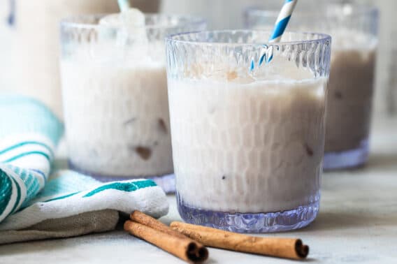 Three glasses of Agua de Horchata with cinnamon sticks in front of them.
