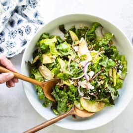 Someone scooping apple walnut salad out of a serving bowl.