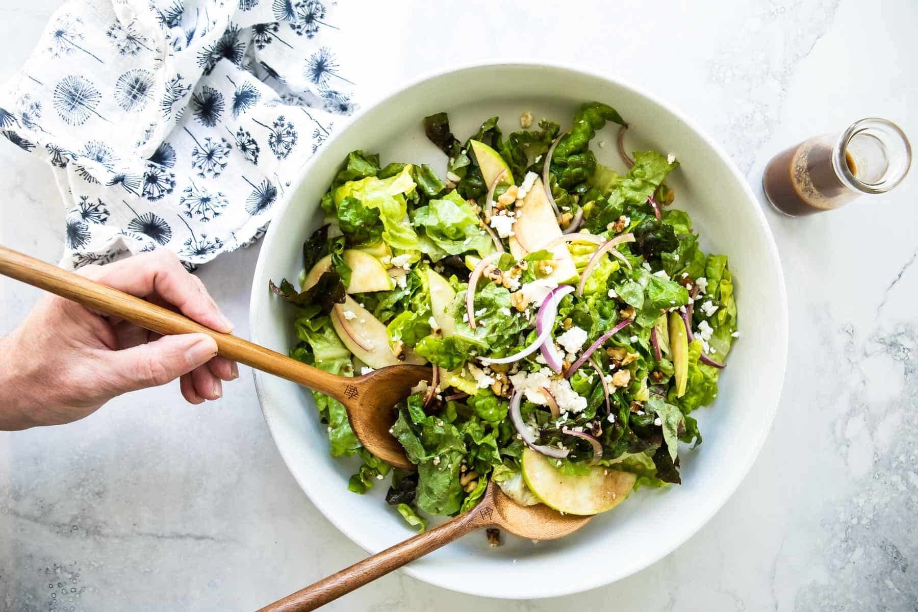 Someone scooping apple walnut salad out of a serving bowl.
