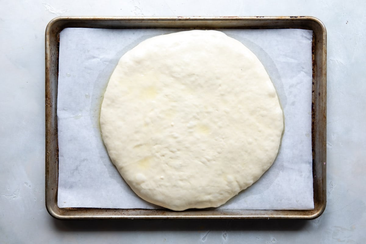 Focaccia bread dough spread out on a baking sheet.