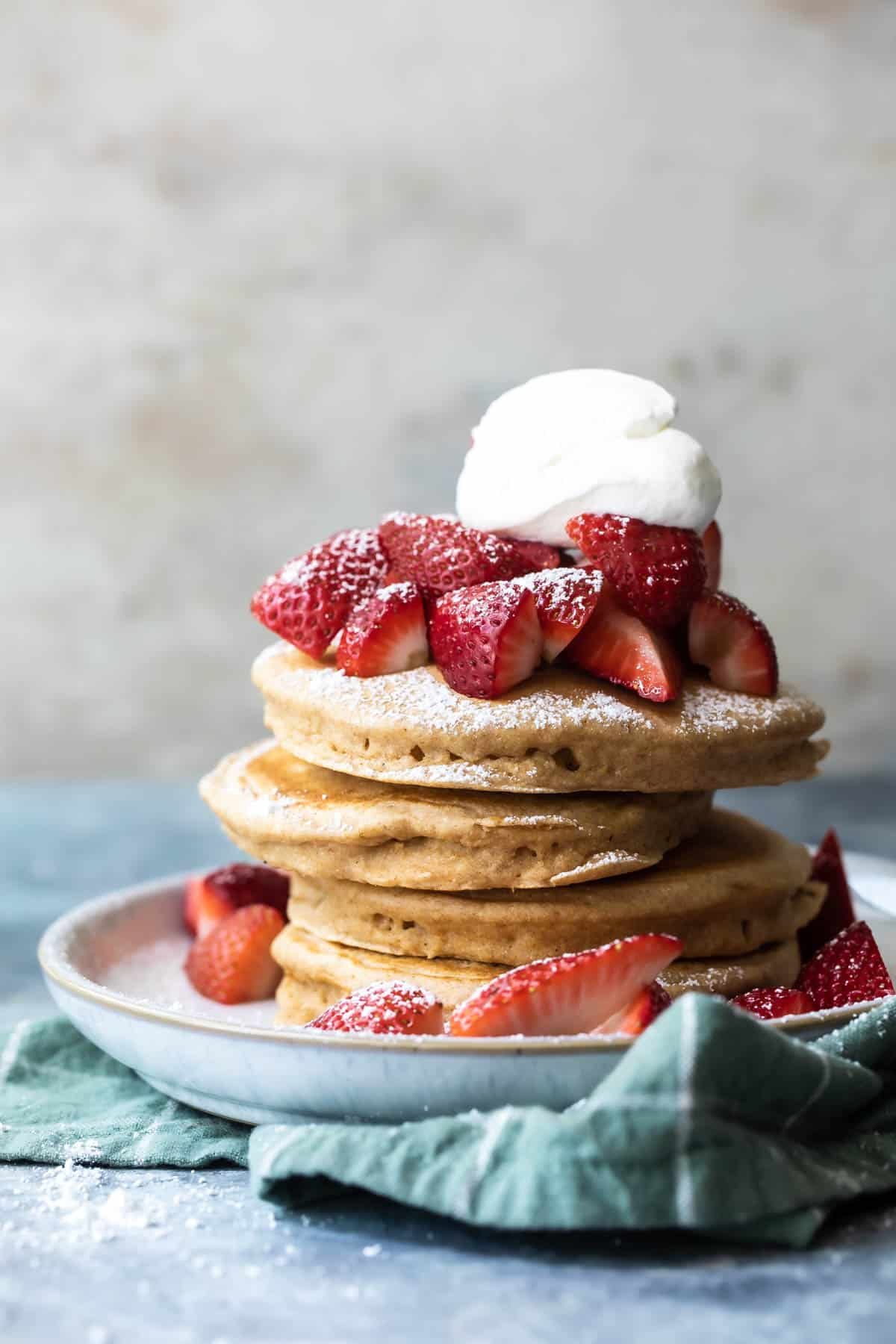 A stack of pancakes with strawberries and whipped cream.