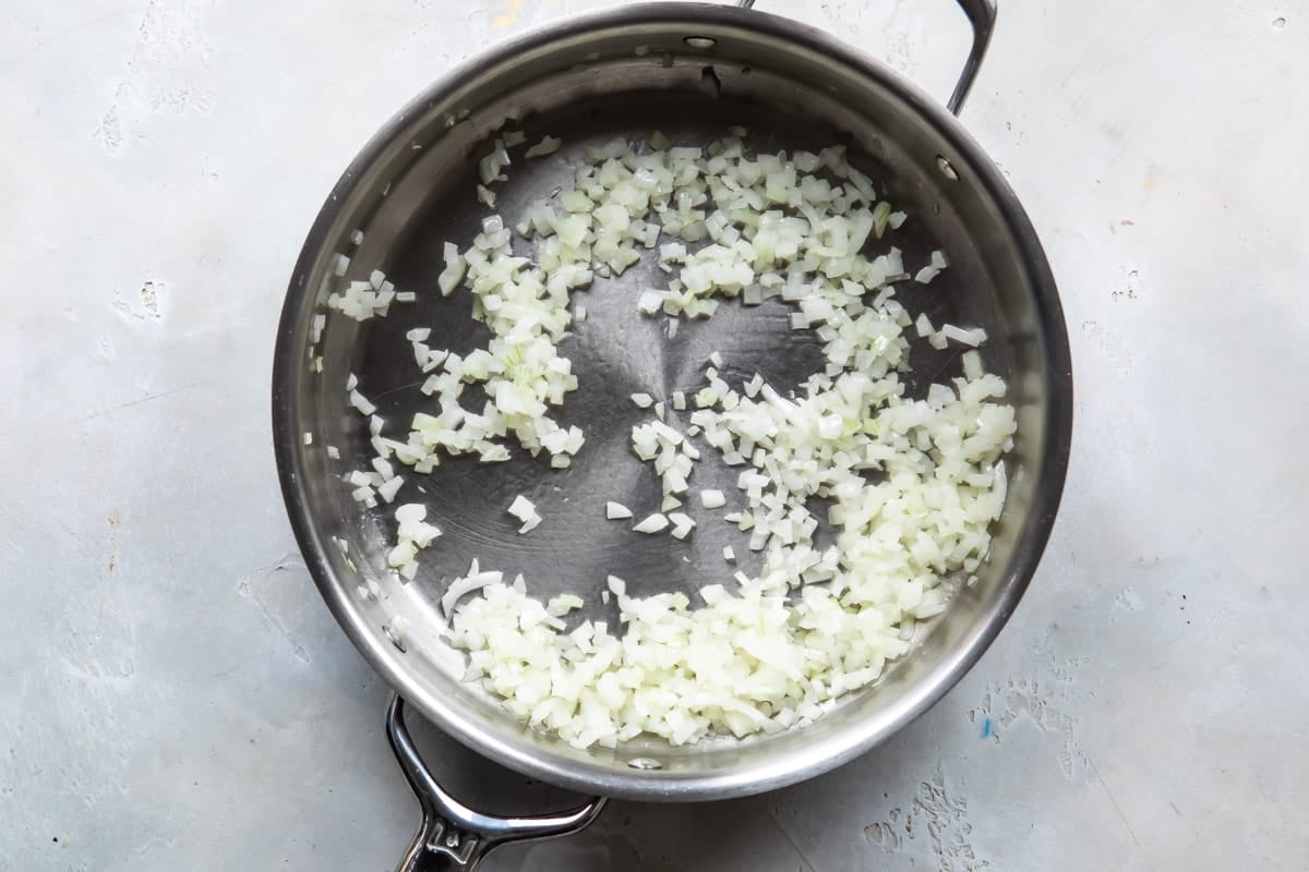 Onion being cooked in a silver skillet.