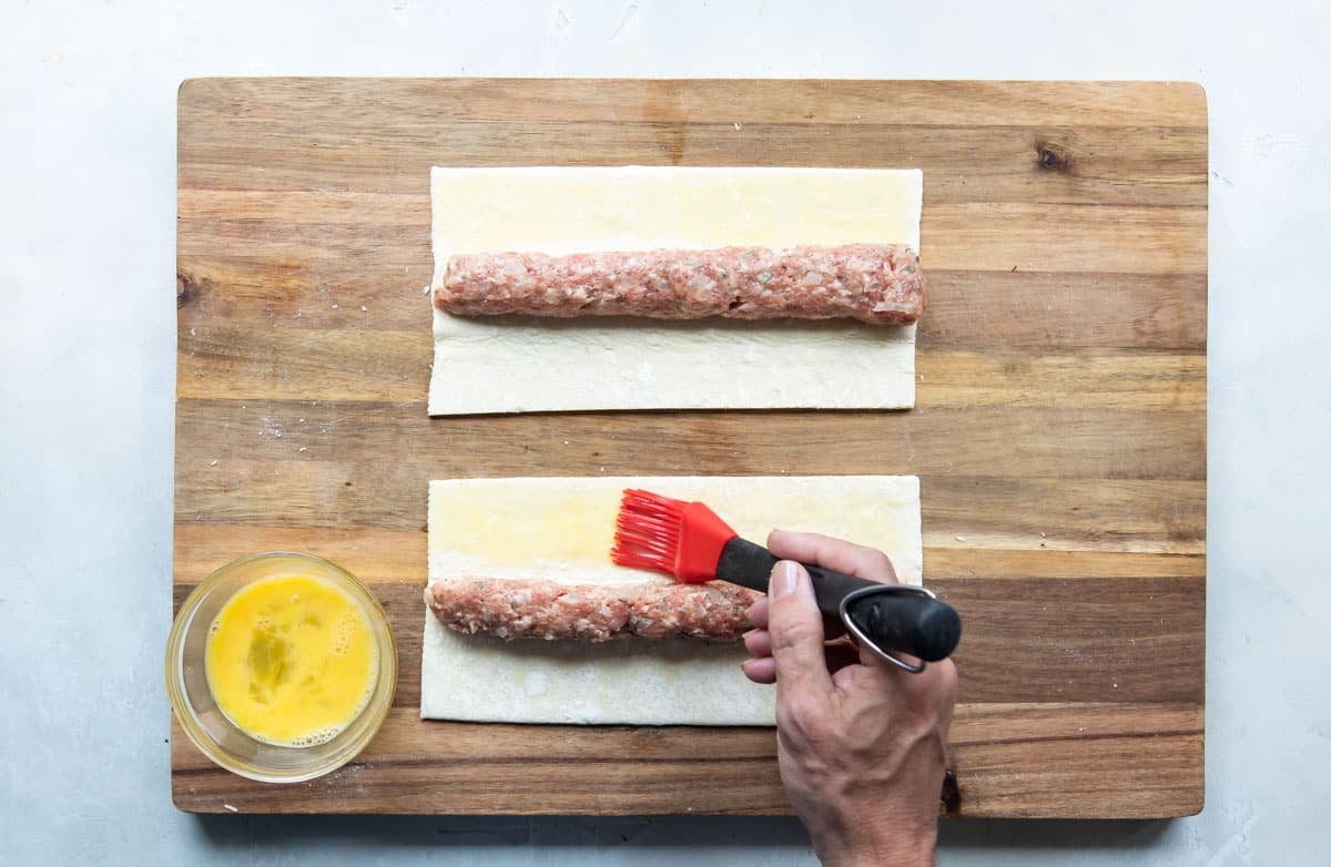Someone brushing sausage rolls with egg wash before rolling them.