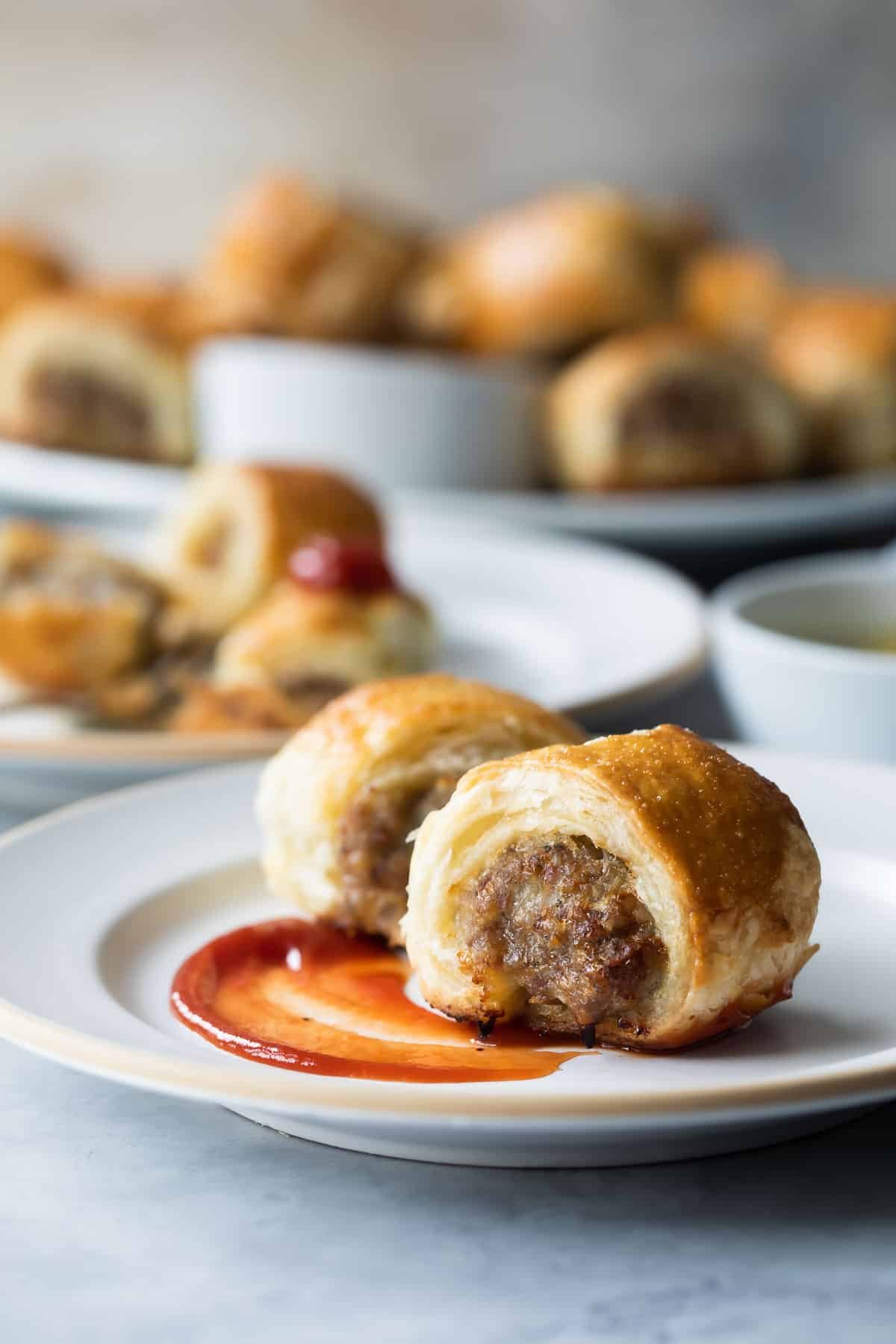 Two sausage rolls on a small white plate with ketchup on it.