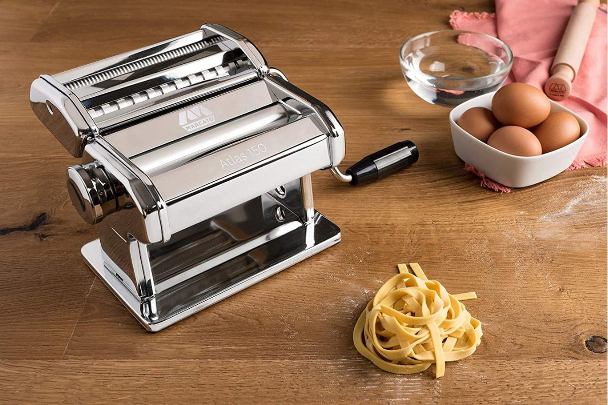 A pasta machine with eggs and noodles on a table