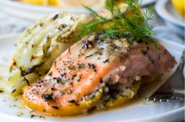 A baked salmon filet on a plate next to roasted fennel.