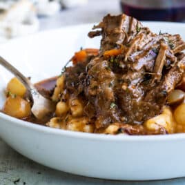 A white bowl of beef bourguignon and mashed potatoes.