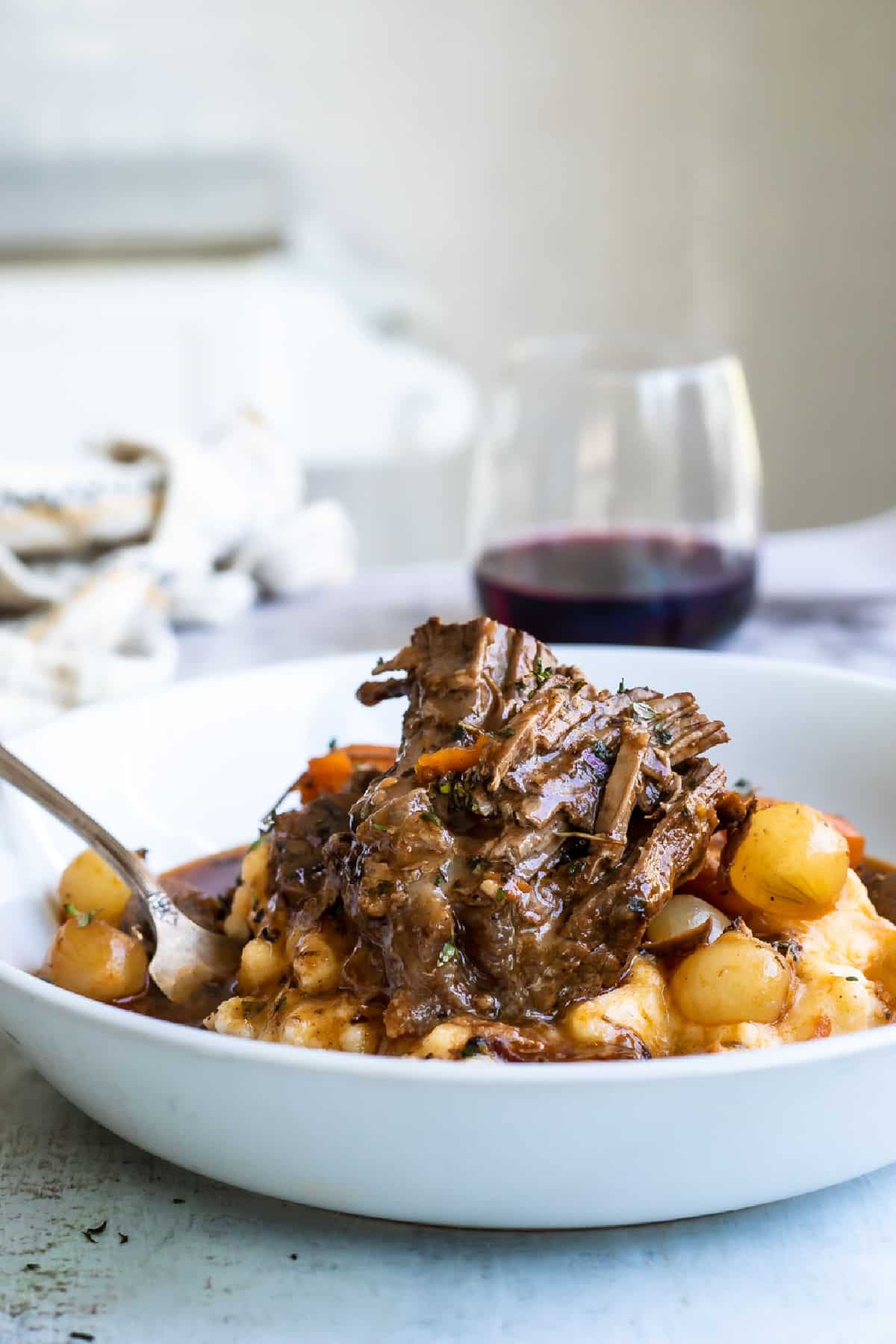 A white bowl of beef bourguignon and mashed potatoes.