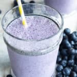 2 glasses of blueberry smoothies next to fresh blueberries.