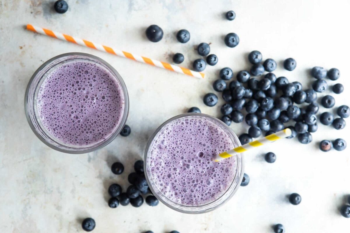 2 glasses of blueberry smoothies next to fresh blueberries.