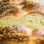 A loaf of Challah with some Challah slices on a wood cutting board.