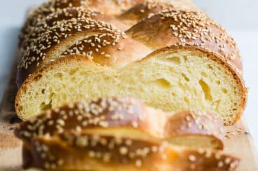 A loaf of Challah with some Challah slices on a wood cutting board.