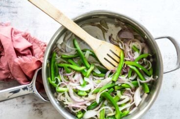 Fajita veggies cooking in a silver skillet with a wooden utensil.