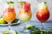 Three granitas on a counter surrounded by garnishes.
