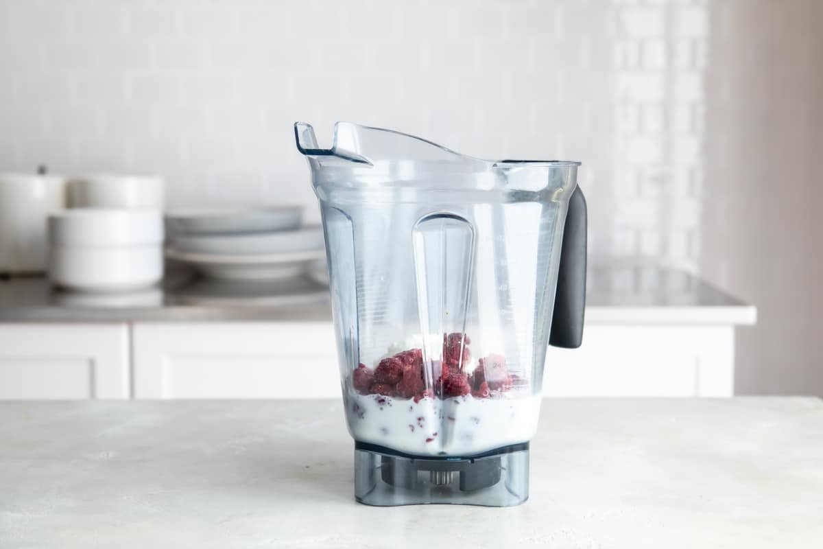 A blender with raspberry smoothie ingredients.
