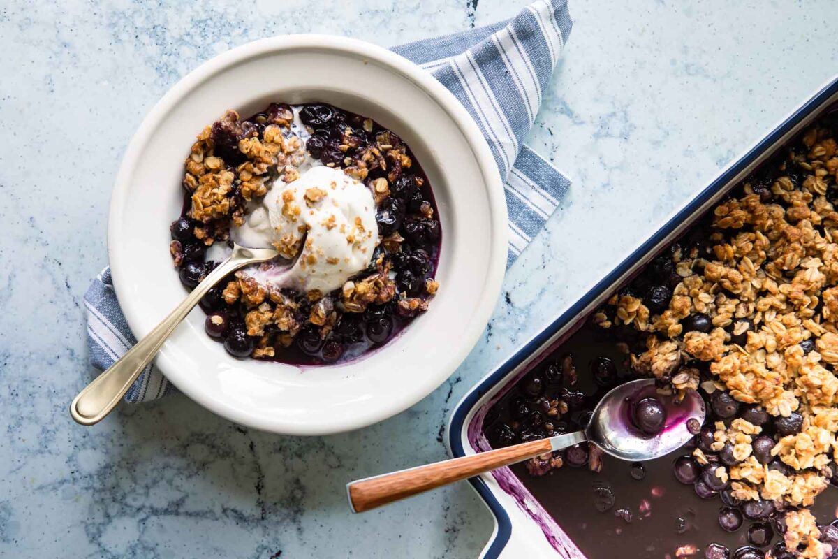 A bowl of blueberry crisp with a scoop of ice cream on top.