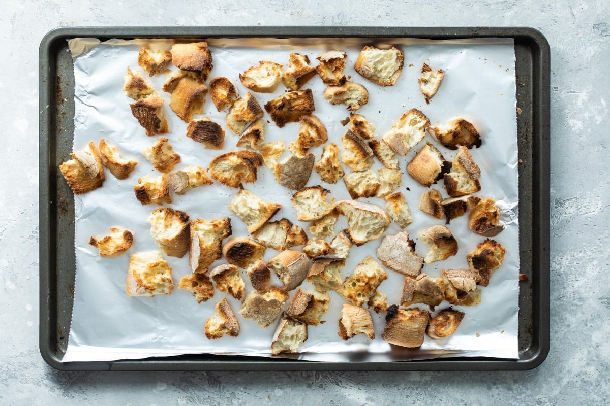 Ripped chunks of bread toasted on a baking sheet lined with tin foil.
