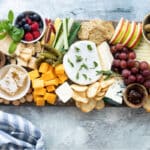 A cheese board filled with fruits, vegetables, nuts, crackers, and cheese.