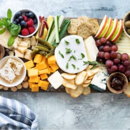 A cheese board filled with fruits, vegetables, nuts, crackers, and cheese.