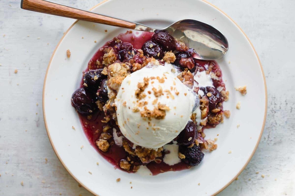 A bowl of cherry crisp with vanilla ice cream on top.
