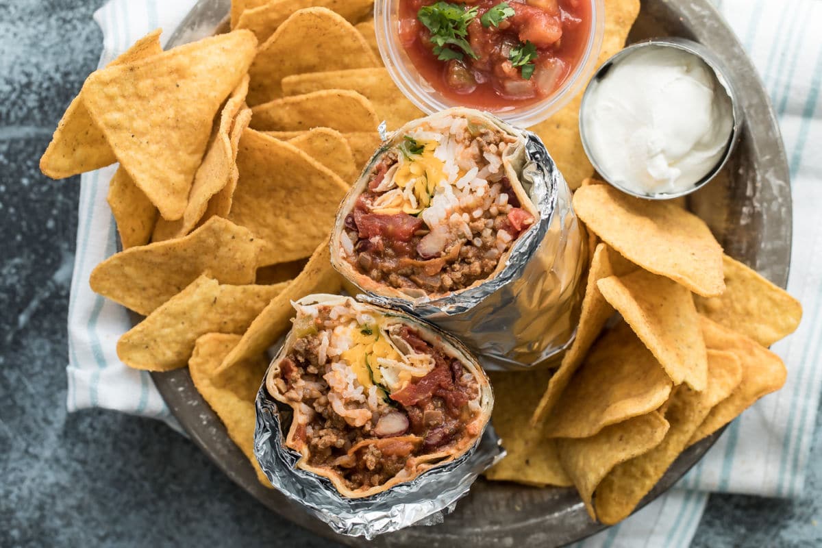 A chili cheese burrito sliced open to show the insides on a pile of tortilla chips.
