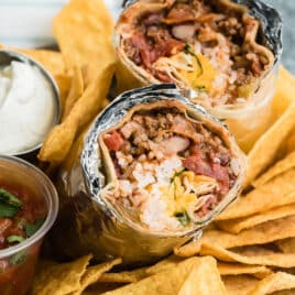 A chili cheese burrito sliced open to show the insides on a pile of tortilla chips.