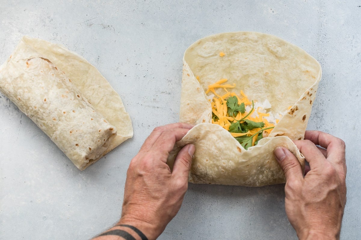 Someone folding up a chili cheese burrito in a flour tortilla.