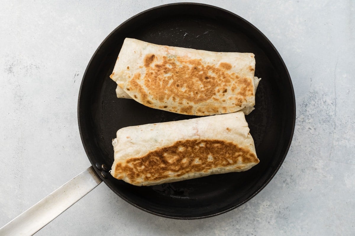 Browning 2 burritos in a skillet.