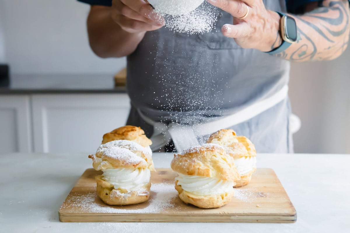 Dusting filled cream puffs with powdered sugar.