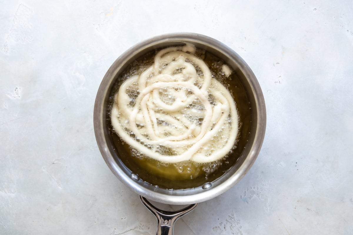 Funnel cakes frying in a pot of oil.