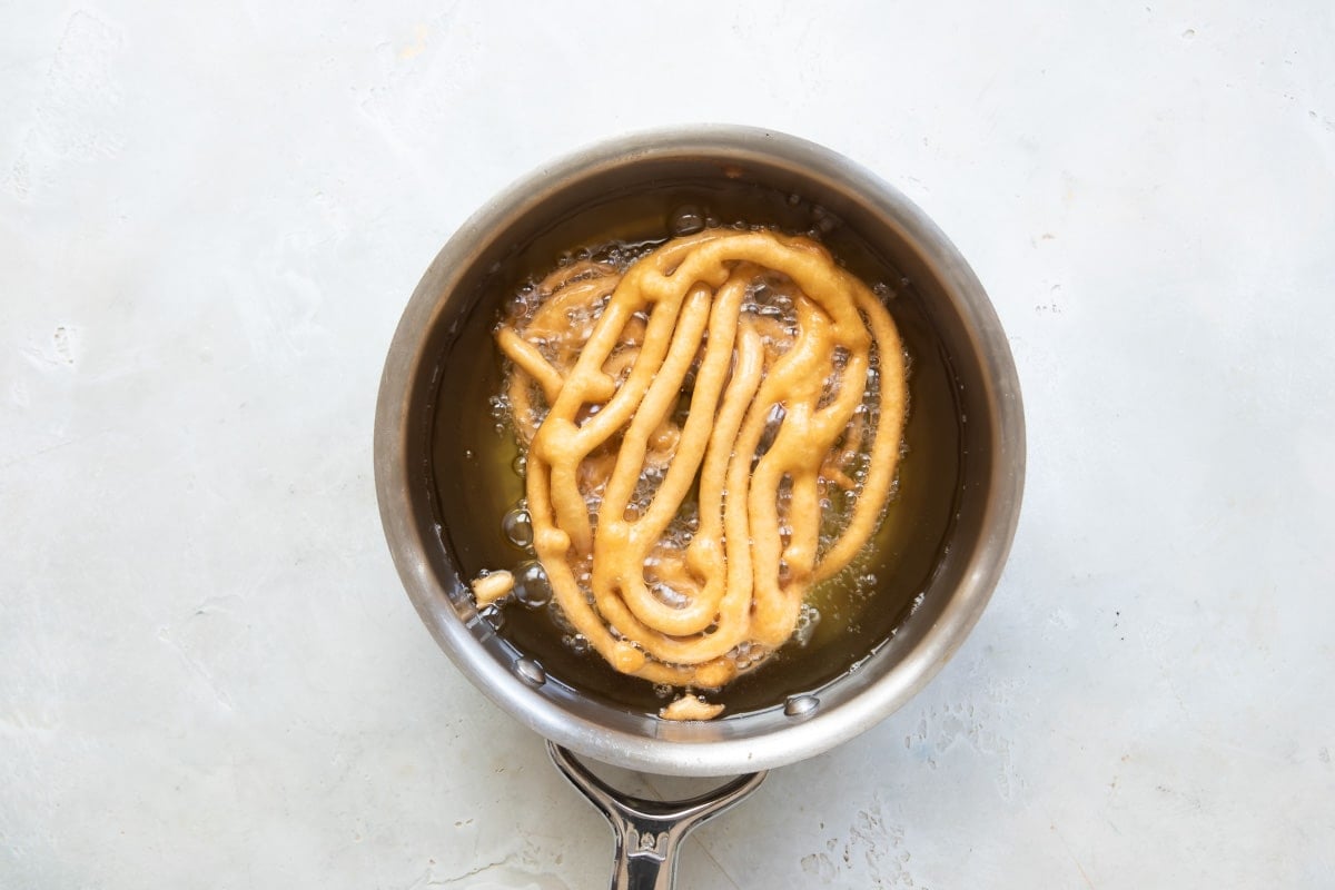 Funnel cakes frying in a pot of oil.