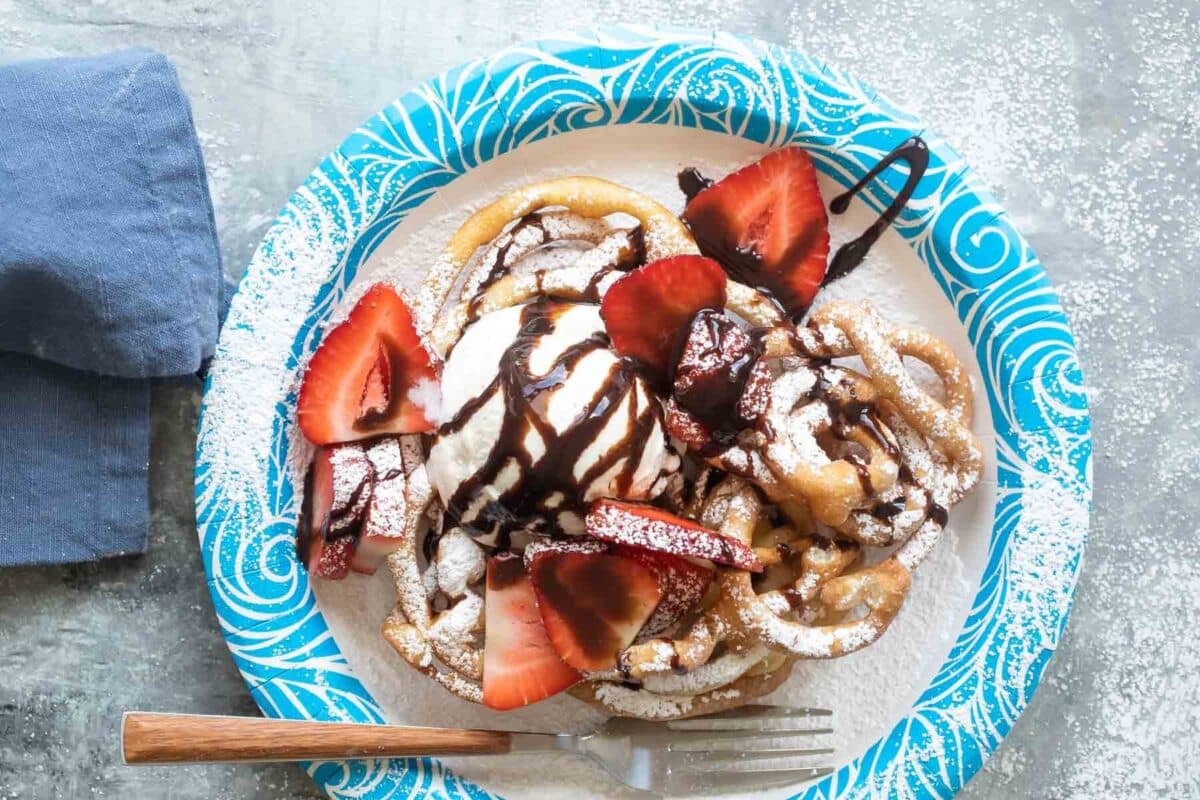 Funnel cakes topped with ice cream, chocolate sauce, and strawberries.