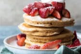 A stack of healthy pancakes with strawberries, whipped cream and powdered sugar.