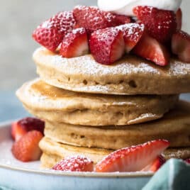 A stack of healthy pancakes with strawberries, whipped cream and powdered sugar.