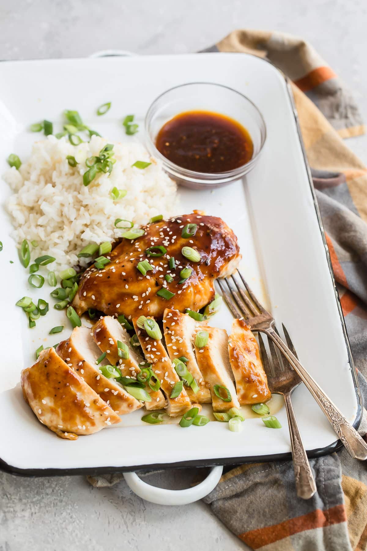 Honey garlic chicken with white rice and a clear bowl of sauce on a white serving platter.
