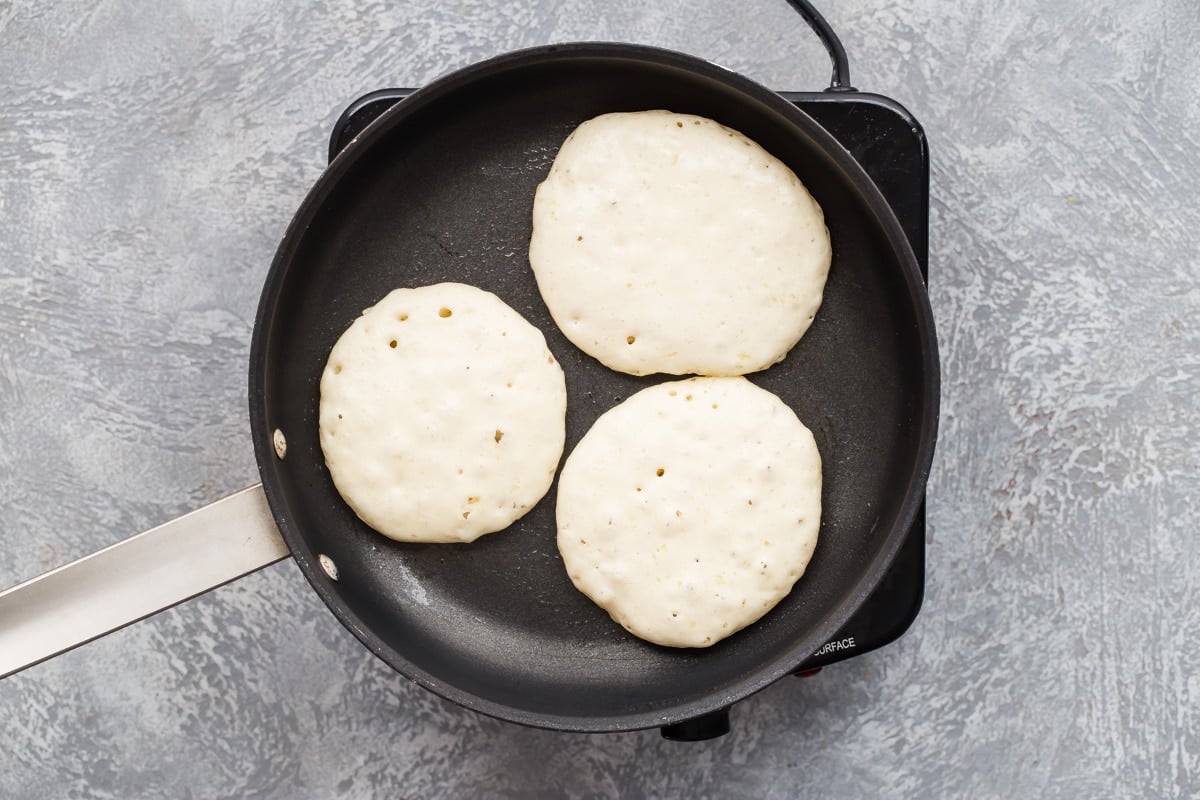 A skillet with 3 lemon ricotta pancakes in it.
