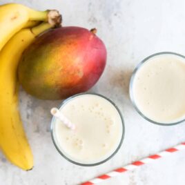Two glasses of mango smoothie next to a mango and some bananas.